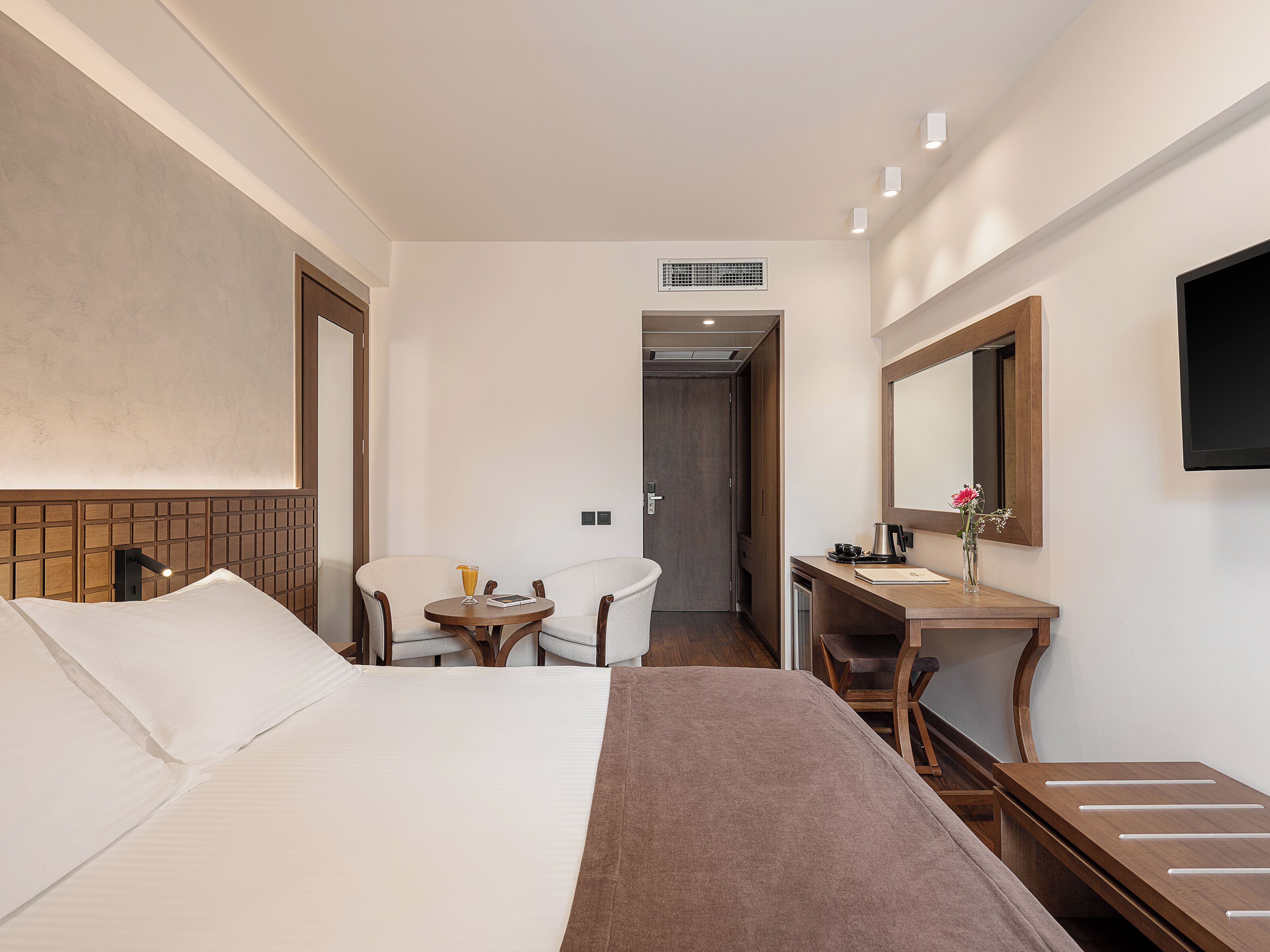 Camera d'albergo con un letto, una scrivania, una sedia, uno specchio e un tavolino con un vaso di fiori.