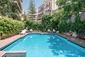 Relax by the serene pool surrounded by lush greenery and a well-maintained hedge, with comfortable lounge chairs and a secure, tiled deck.