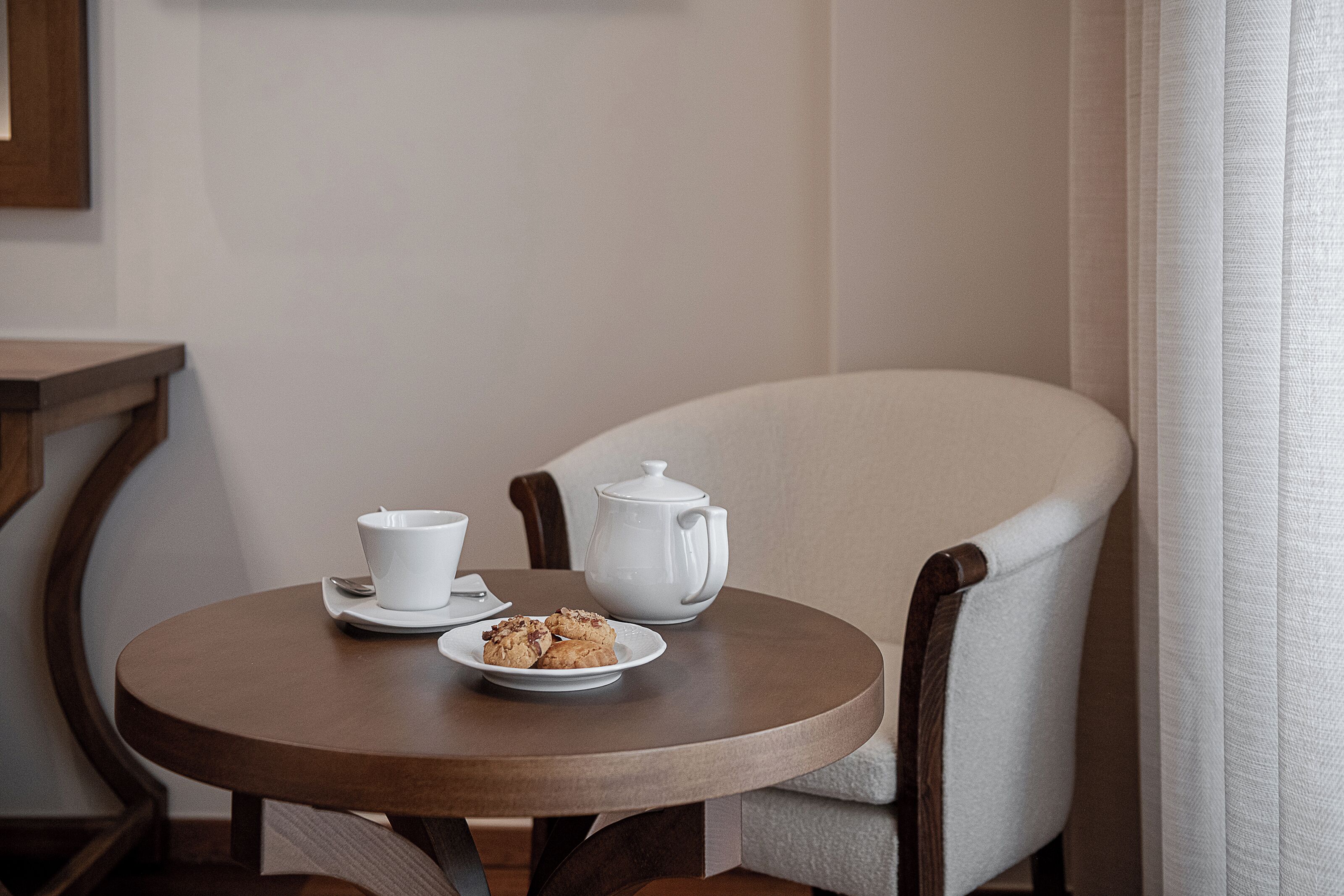 A round wooden table with a white teapot, a white cup, and a plate of cookies.