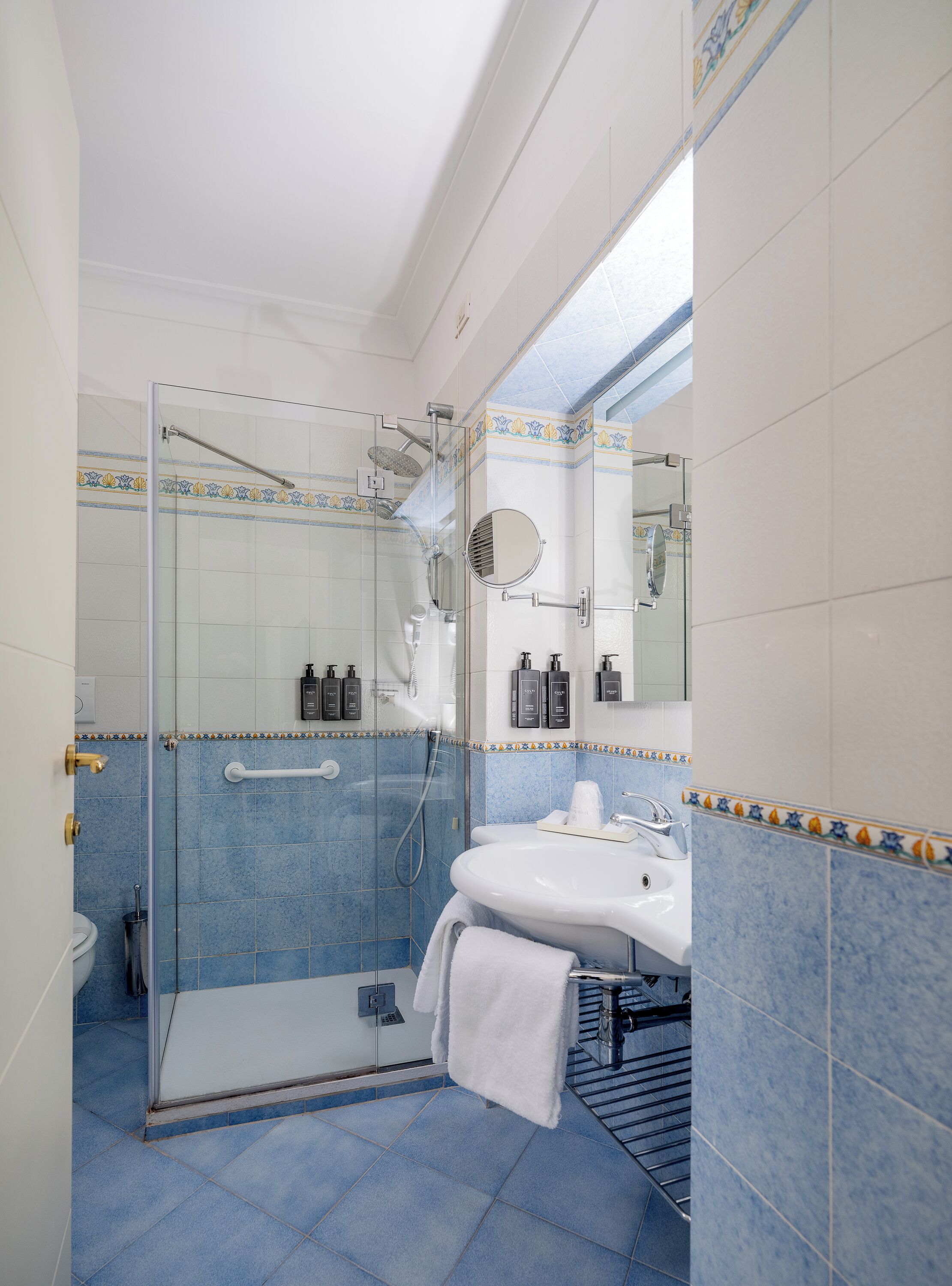 Une salle de bain avec une douche à parois de verre, un lavabo avec un miroir et des murs recouverts de carreaux bleus.