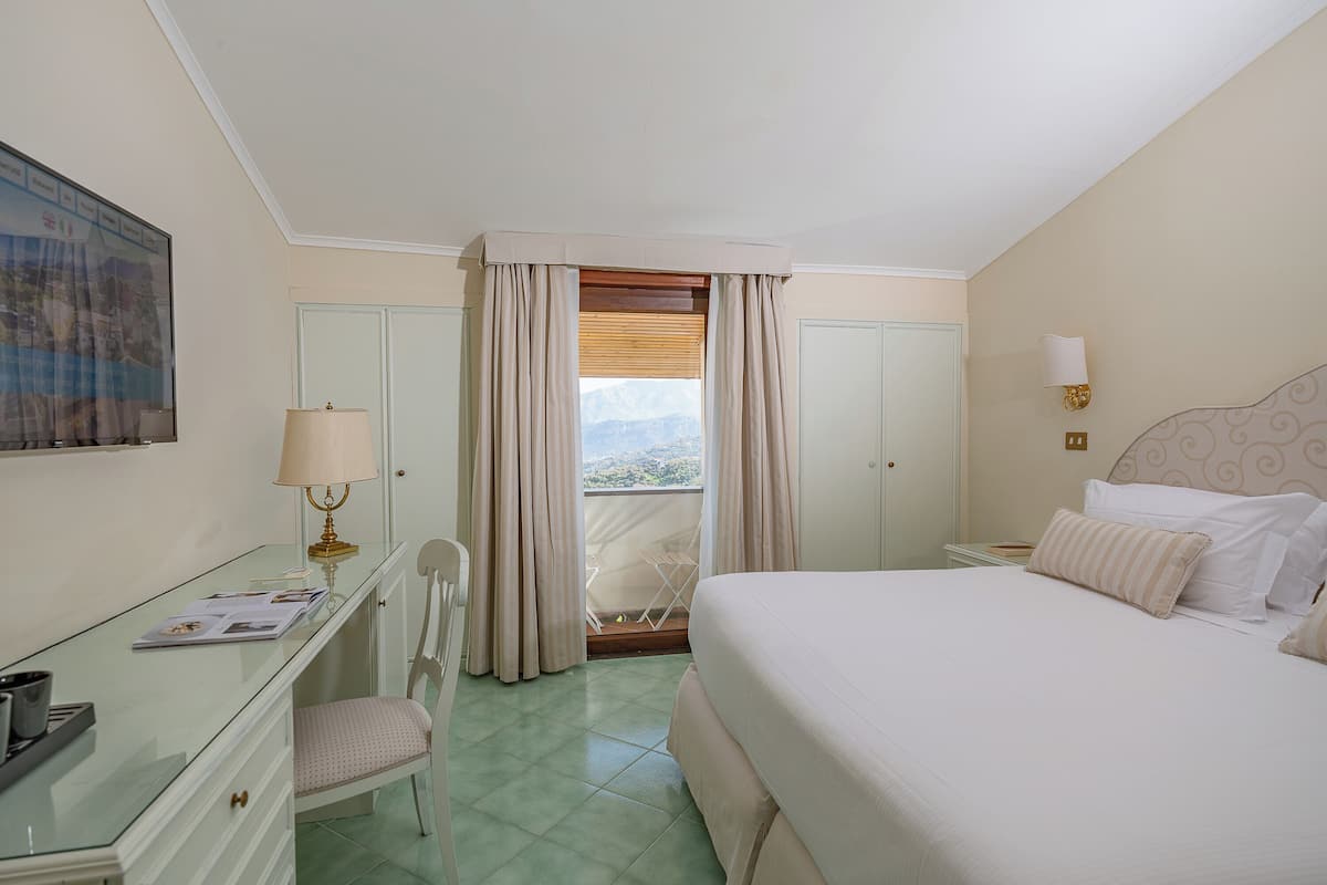 Une chambre d’hôtel comprenant un lit, un bureau, une chaise, une fenêtre avec des rideaux et une vue sur l’extérieur.