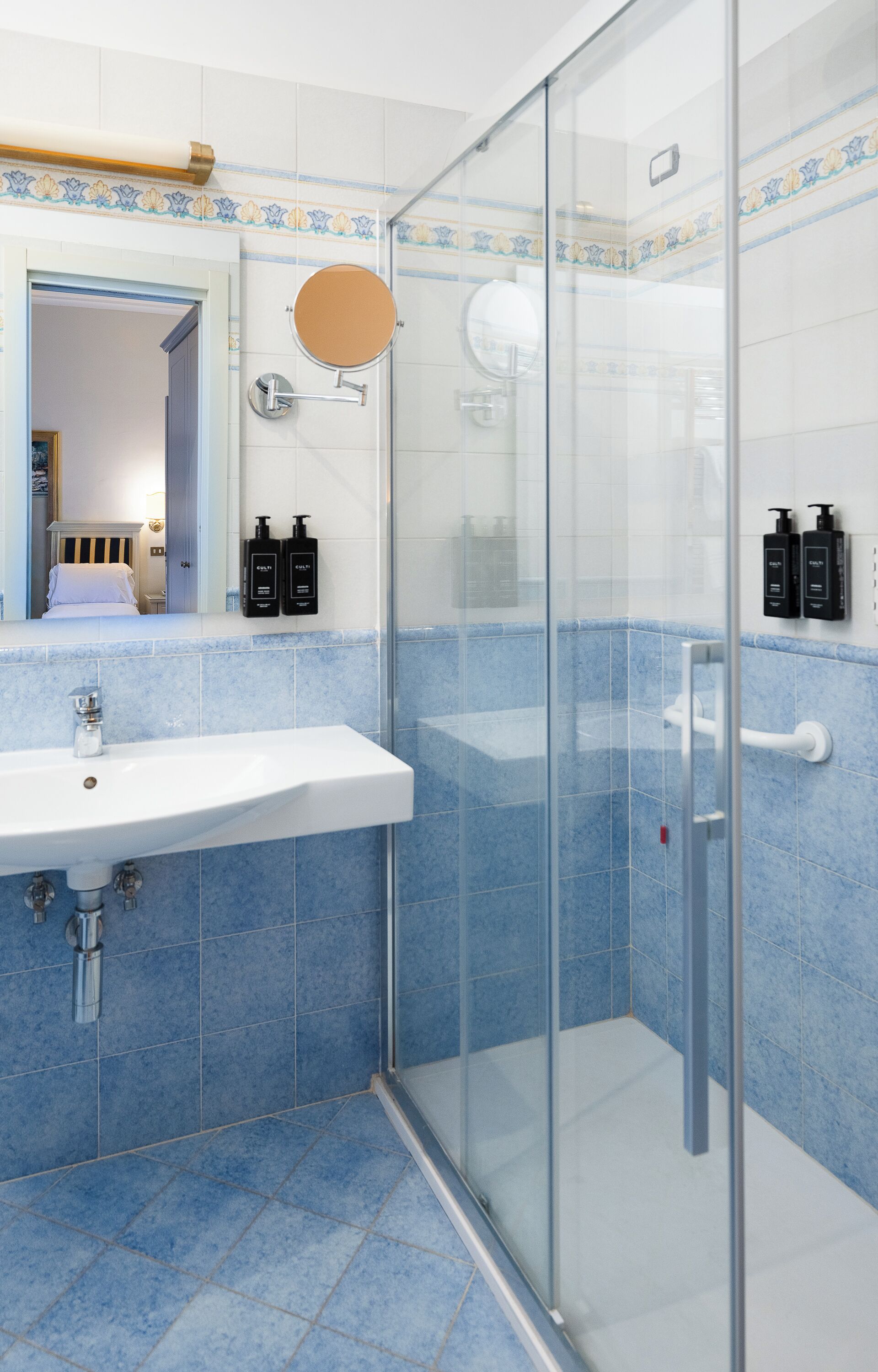 A bathroom with a glass shower enclosure, a sink with a mirror, and toiletries on the wall.