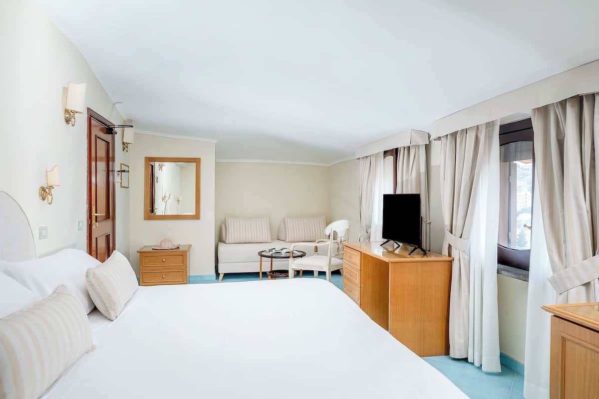 Une chambre d’hôtel avec un grand lit, un bureau avec une télévision, une chaise, un canapé et un miroir.