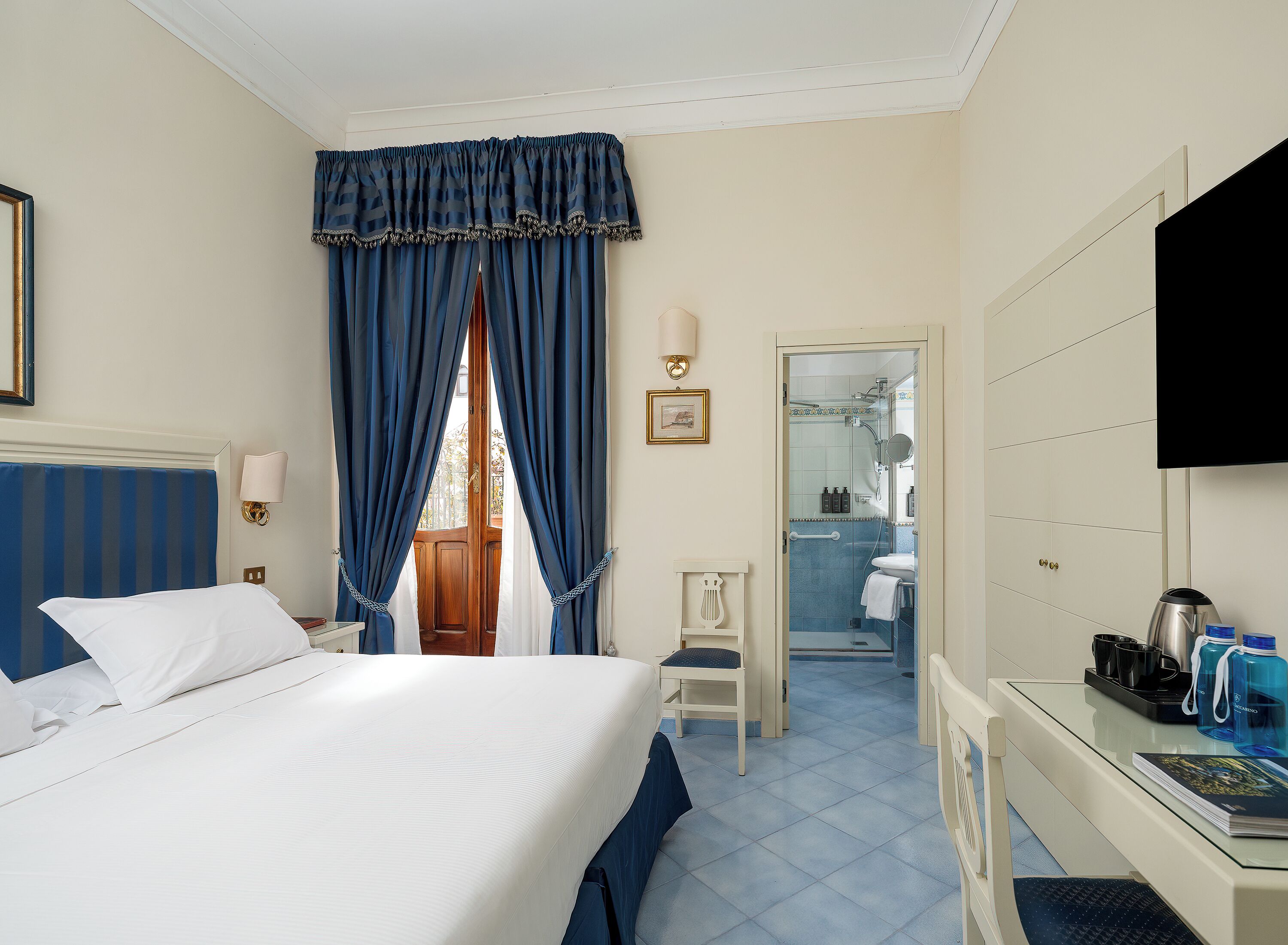 Habitación de hotel con cama, escritorio con computadora, silla, baño con ducha y televisor.