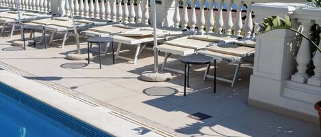 A poolside area with sun loungers, umbrellas, and a lamp post.