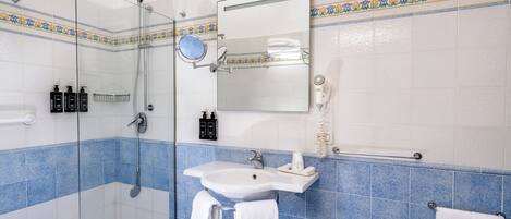 A bathroom with a glass shower enclosure, a sink, a mirror, and a hairdryer.