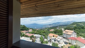 Uitzicht vanaf een balkon op een kustplaatsje met gebouwen, een weg en bergen in de verte.
