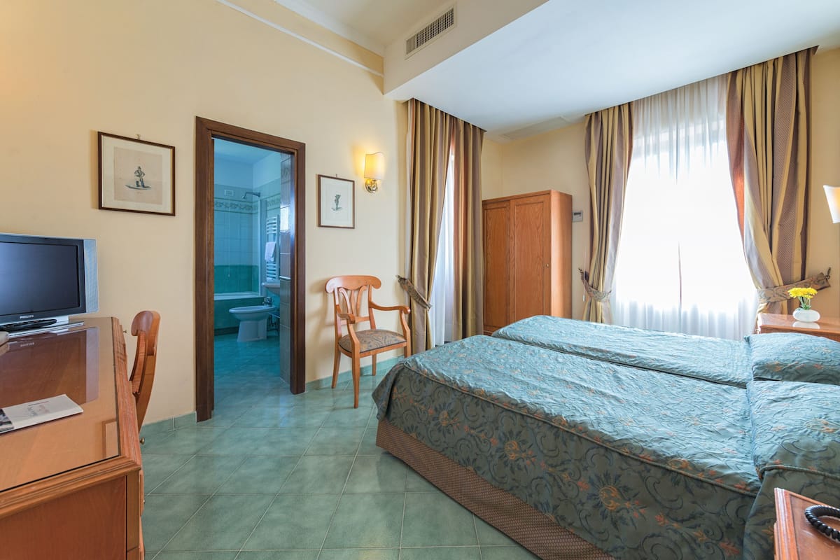 Une chambre d’hôtel avec un lit, un bureau, une chaise, une télévision et une salle de bain visible à travers une porte ouverte.