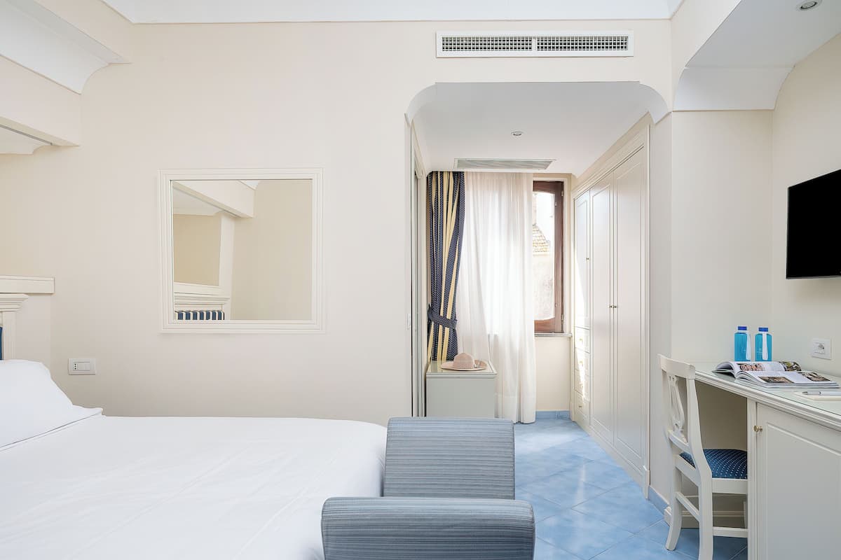 Une chambre d’hôtel avec un lit, un bureau et une chaise, un miroir et un téléviseur fixé au mur.