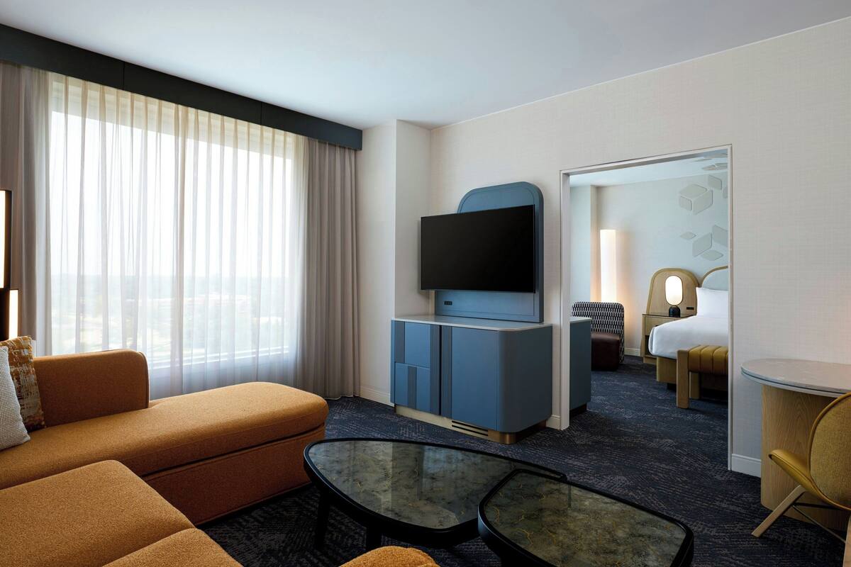 A hotel room with a sofa, a TV, a small table, a bed, and a desk with a lamp.