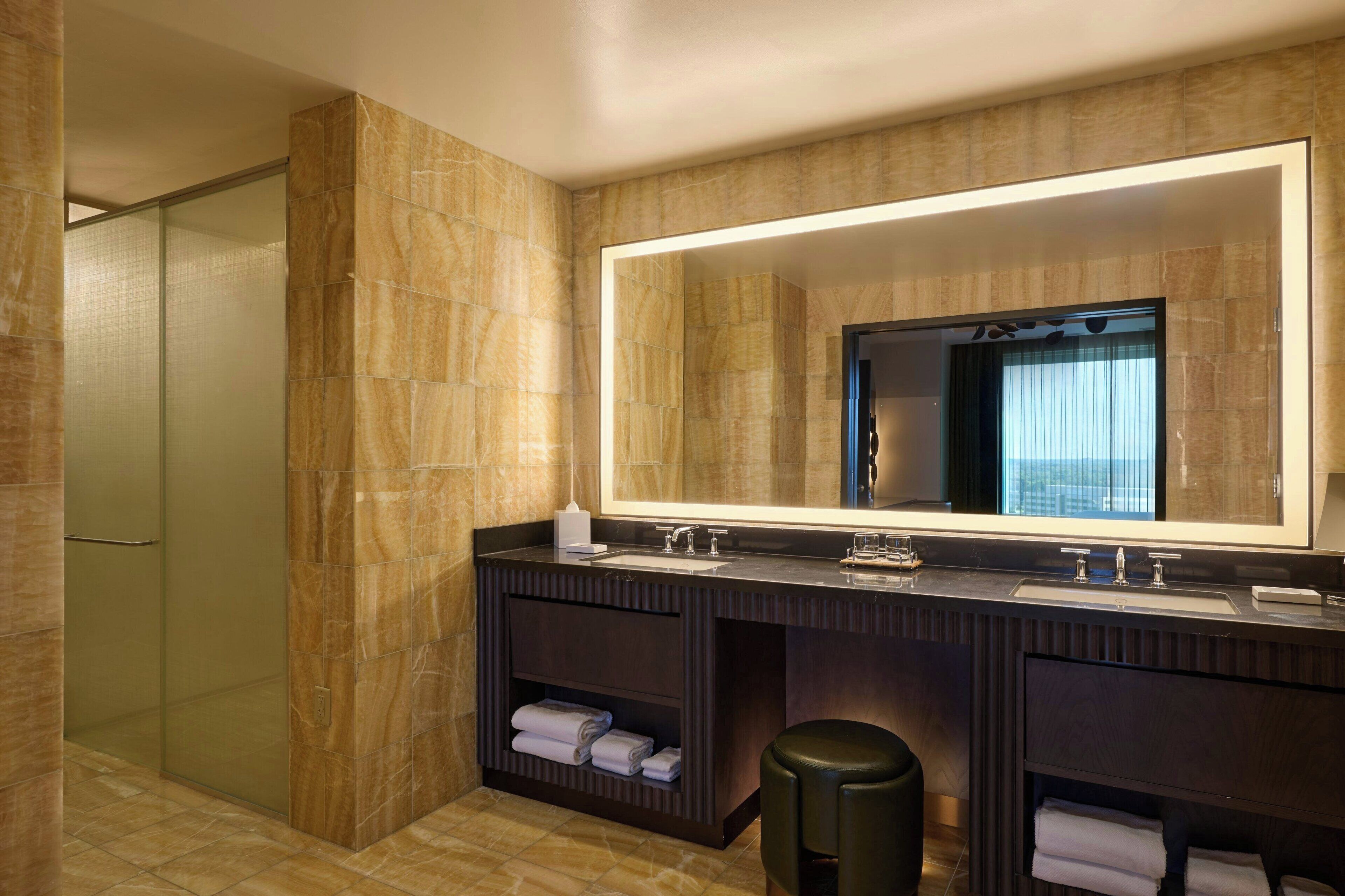 A modern bathroom with a large mirror, two sinks, and a shower area.
