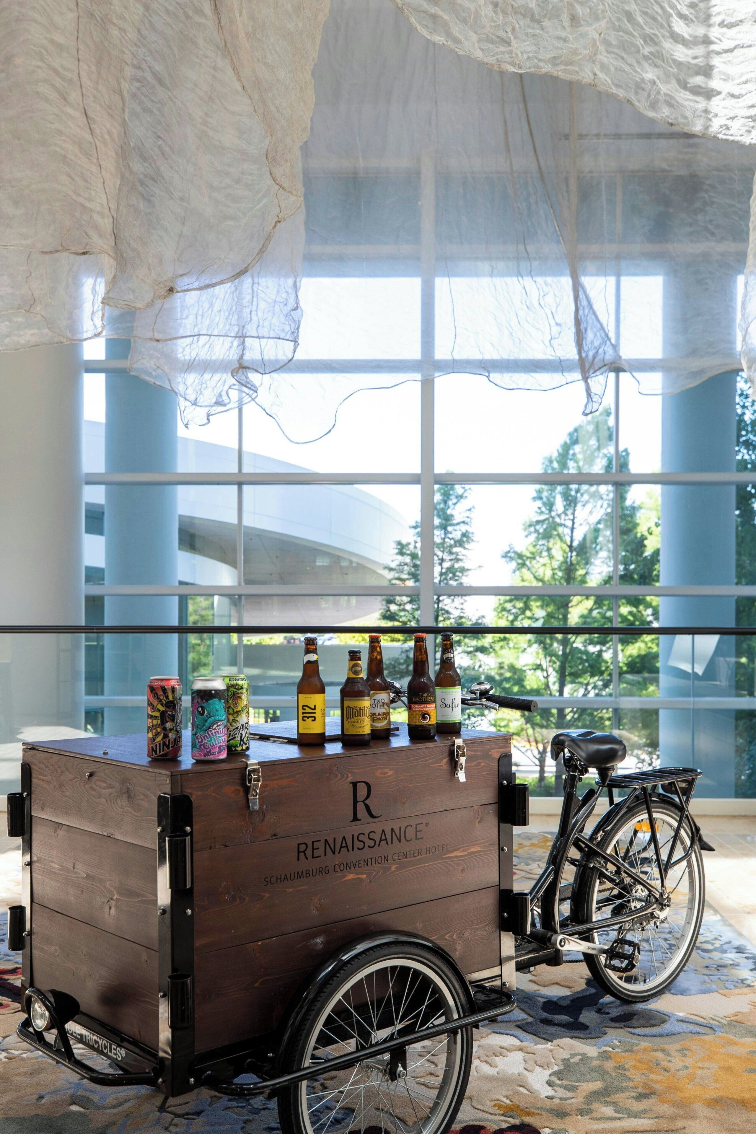 En trækasse med en cykel parkeret ved siden af, indeholdende flasker og dåser, i et rummeligt rum med store vinduer.