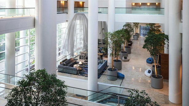 Ein mehrgeschossiges Atrium mit Glastrennvorrichtungen, großen weißen Säulen und Pflanzgefäßen.