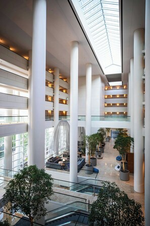 Un atrium à plusieurs niveaux, doté de rampes en verre, de grandes colonnes blanches et de plantes en pot.
