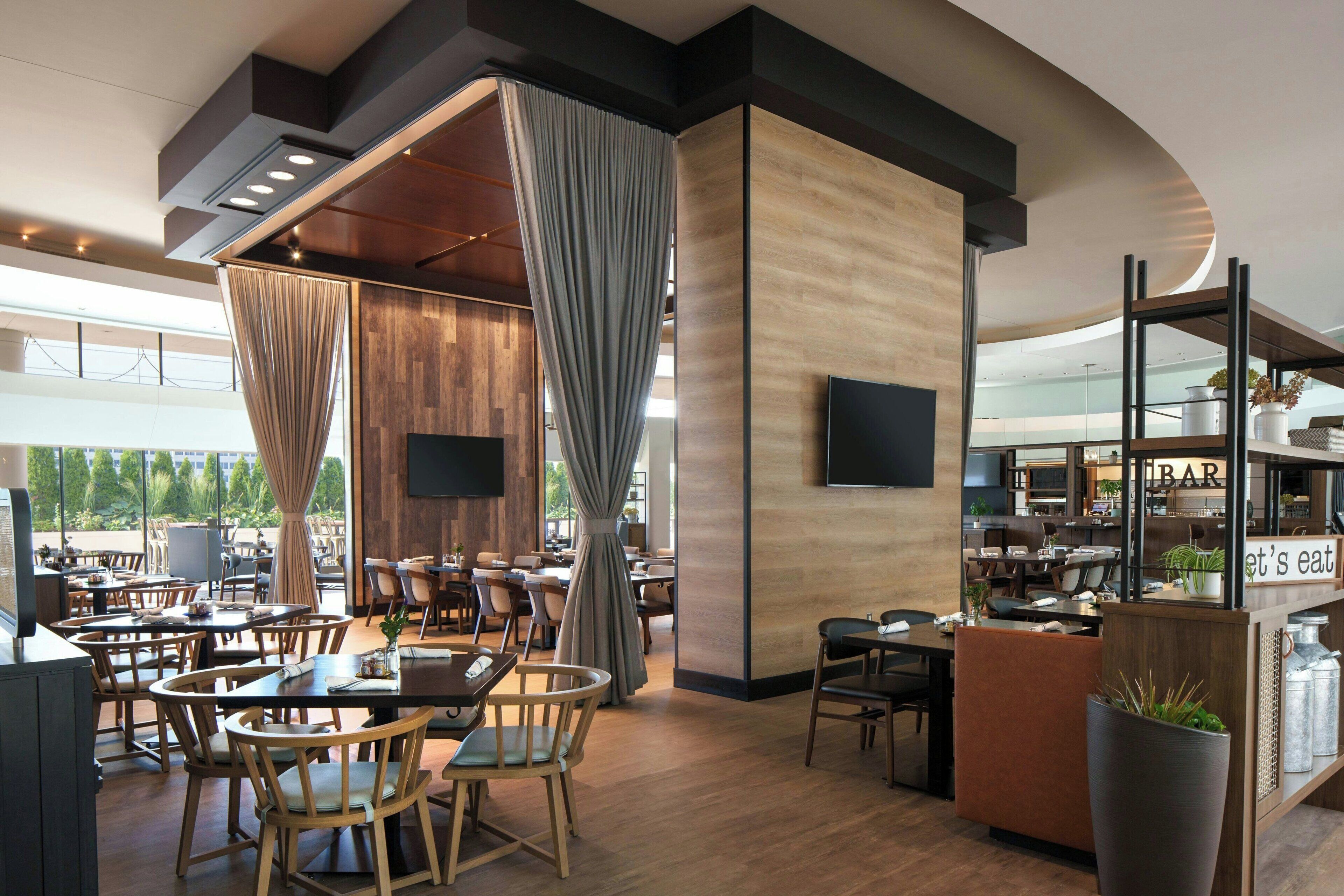 Un restaurante moderno con suelo de madera, una zona de bar y un amplio ventanal con vistas al exterior.