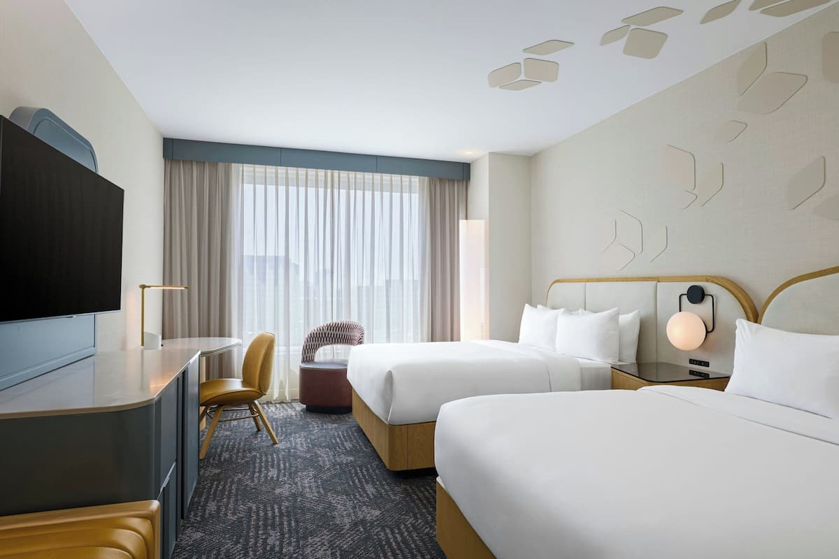 A hotel room with two beds, a desk, a chair, and a TV.
