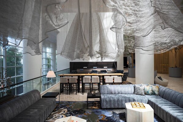 Un salon moderne avec un canapé gris, un tapis à motifs et un coin repas comprenant une table et des chaises en bois.