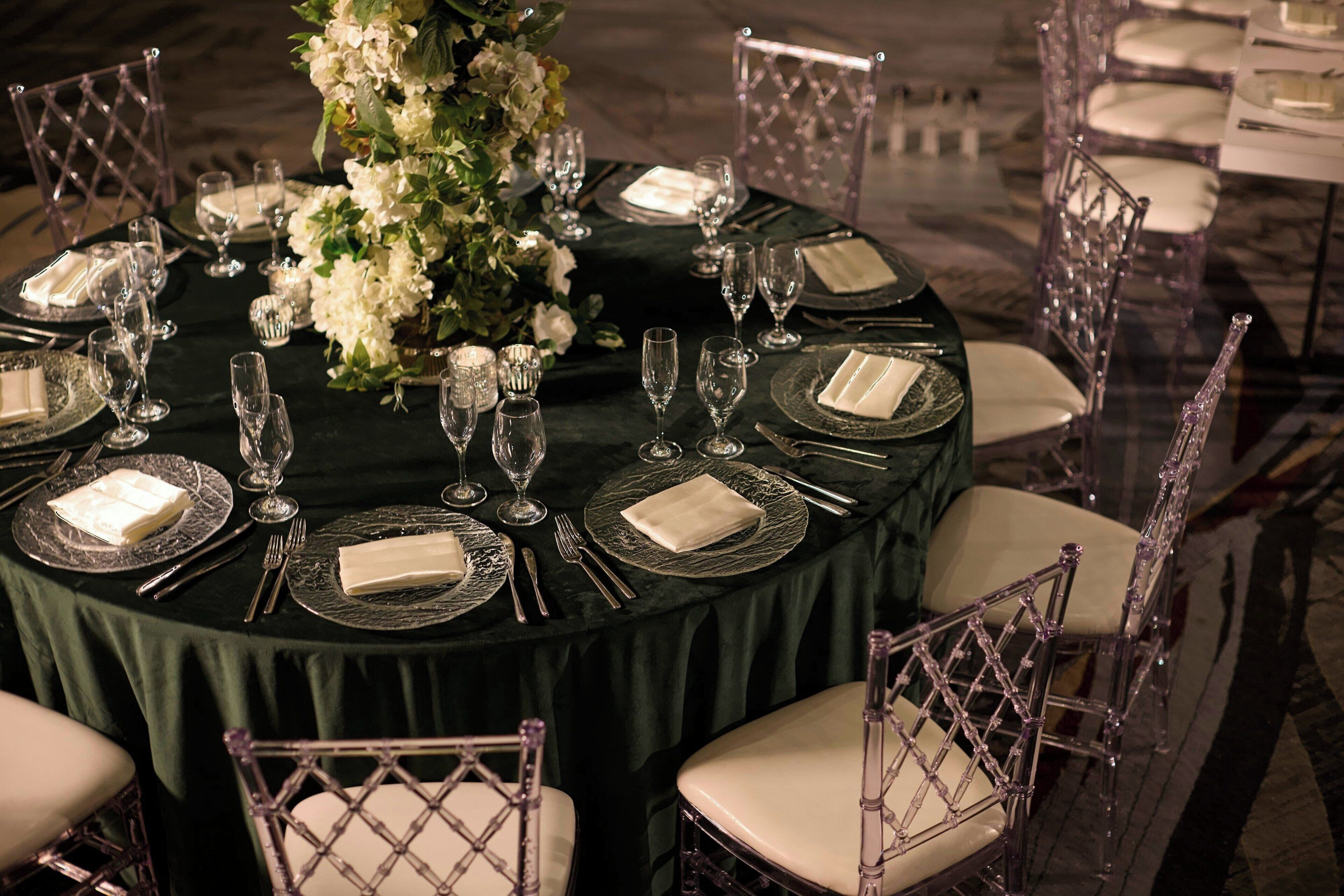A round table set for a formal dinner with clear glassware, folded napkins, and a floral centerpiece.