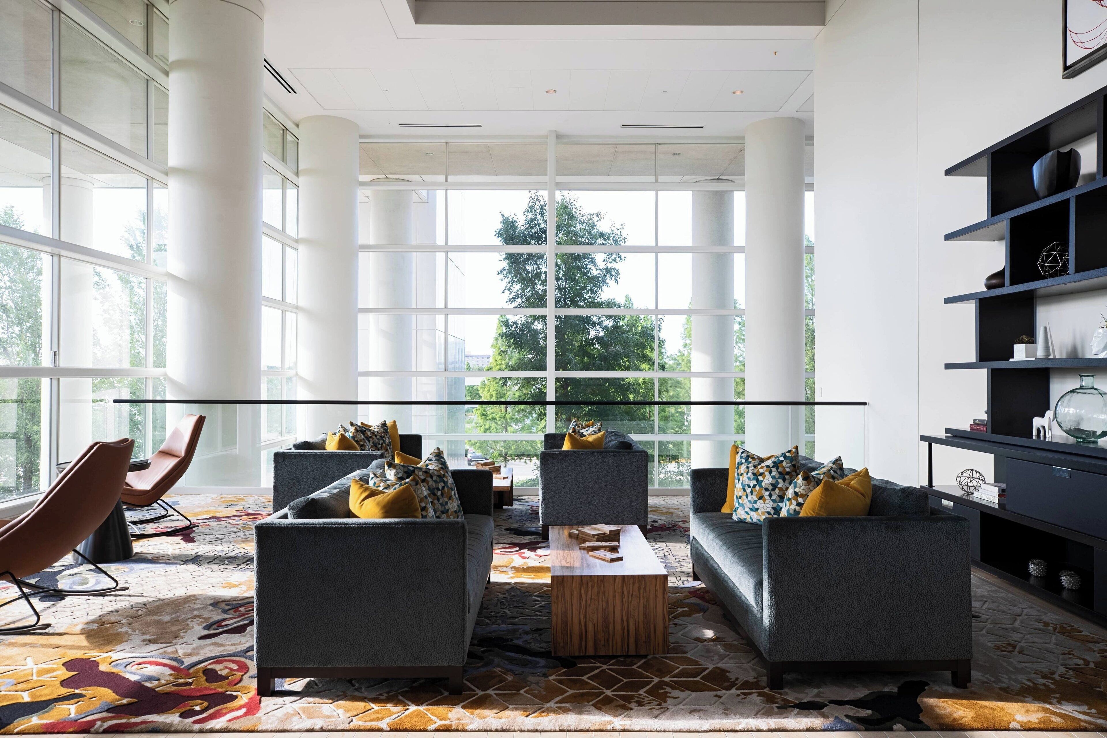 Un espace détente moderne doté de grandes fenêtres, de deux canapés avec des coussins, d’une table basse et d’une bibliothèque.