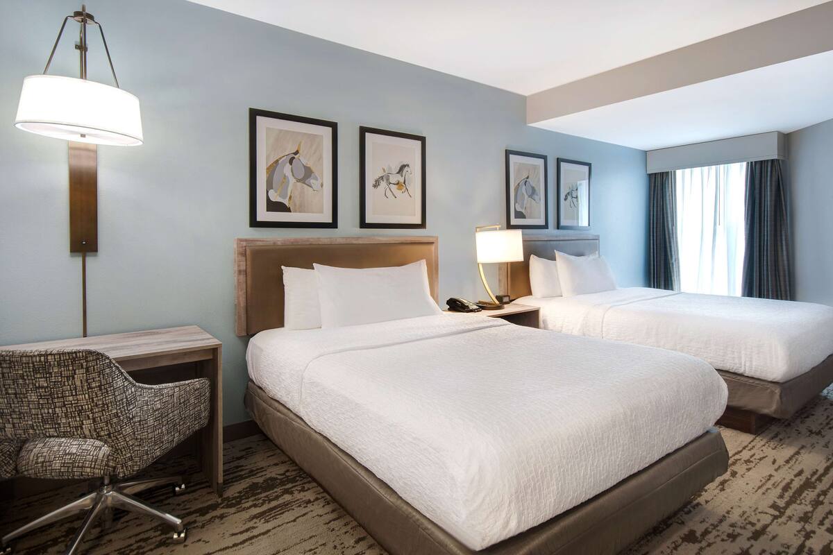 A hotel room with two beds, a desk, a chair, and artwork on the walls.