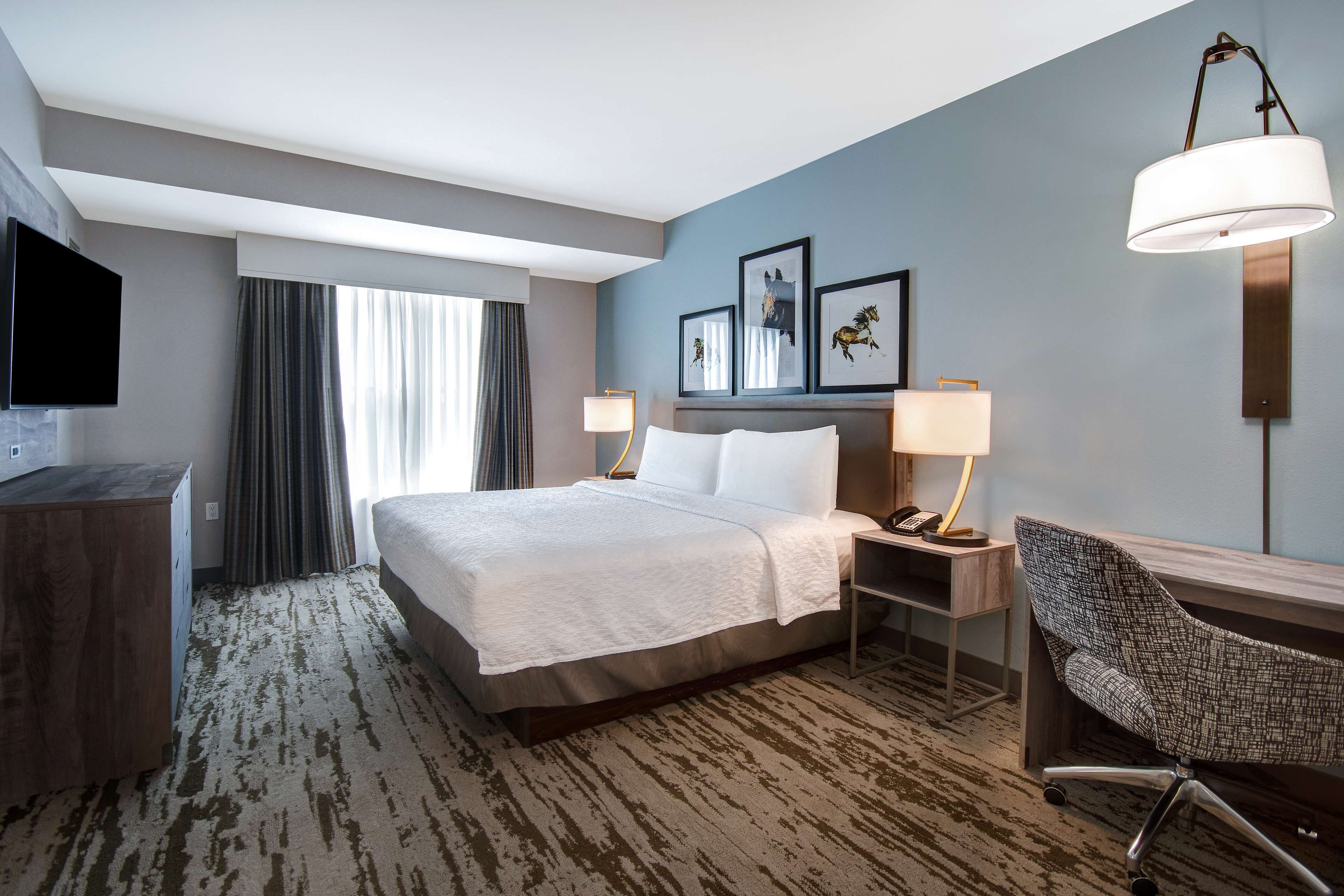 Ein Hotelzimmer mit einem großen Bett, einem Schreibtisch mit Stuhl, einem Fernseher und Kunstwerken an der Wand.
