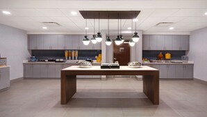 Une cuisine moderne avec des meubles de couleur grise, une table à manger en bois et un éclairage suspendu au plafond.