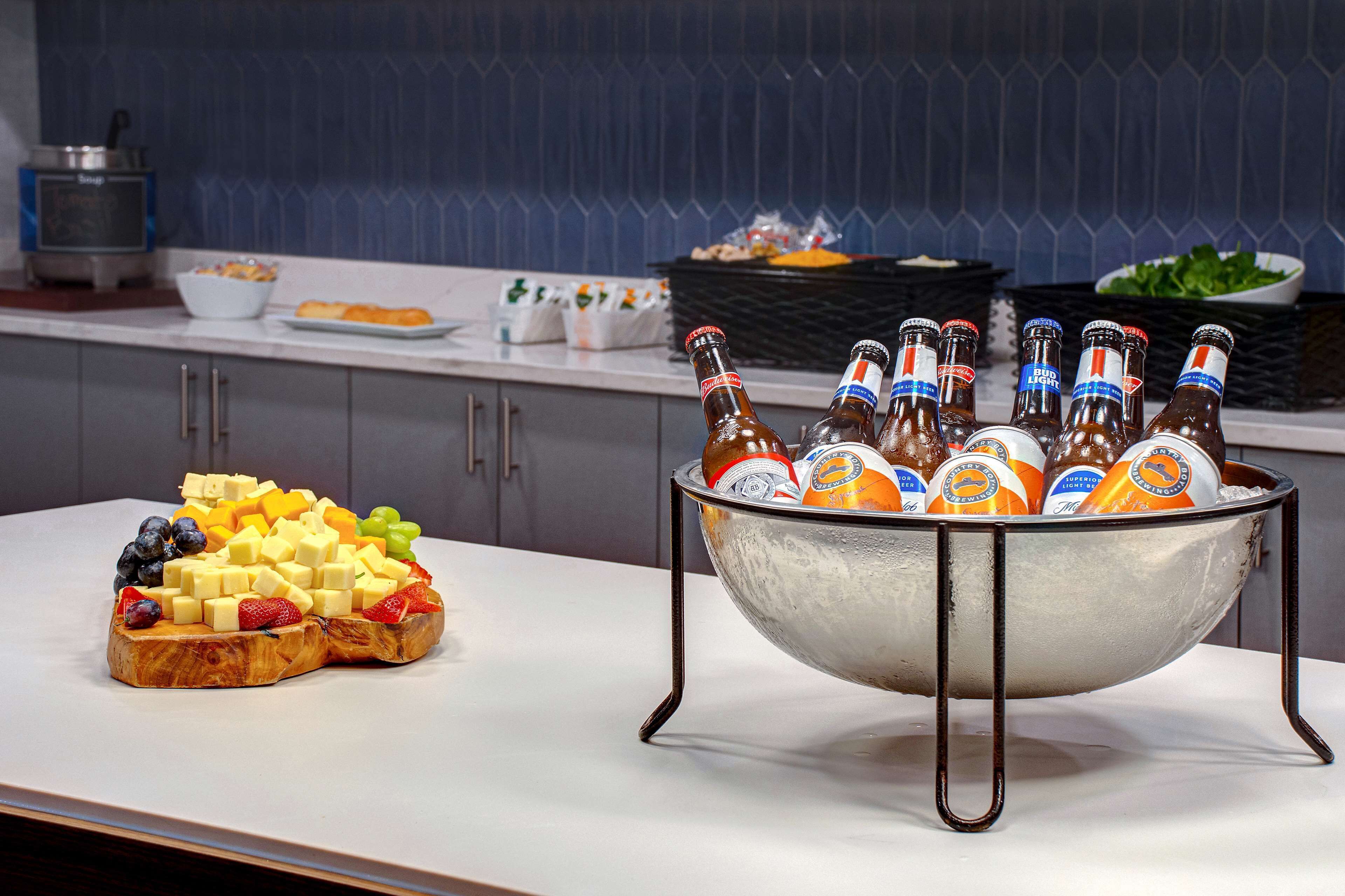 A kitchen counter with a fruit and cheese platter, a bowl of beer bottles, and a kettle.