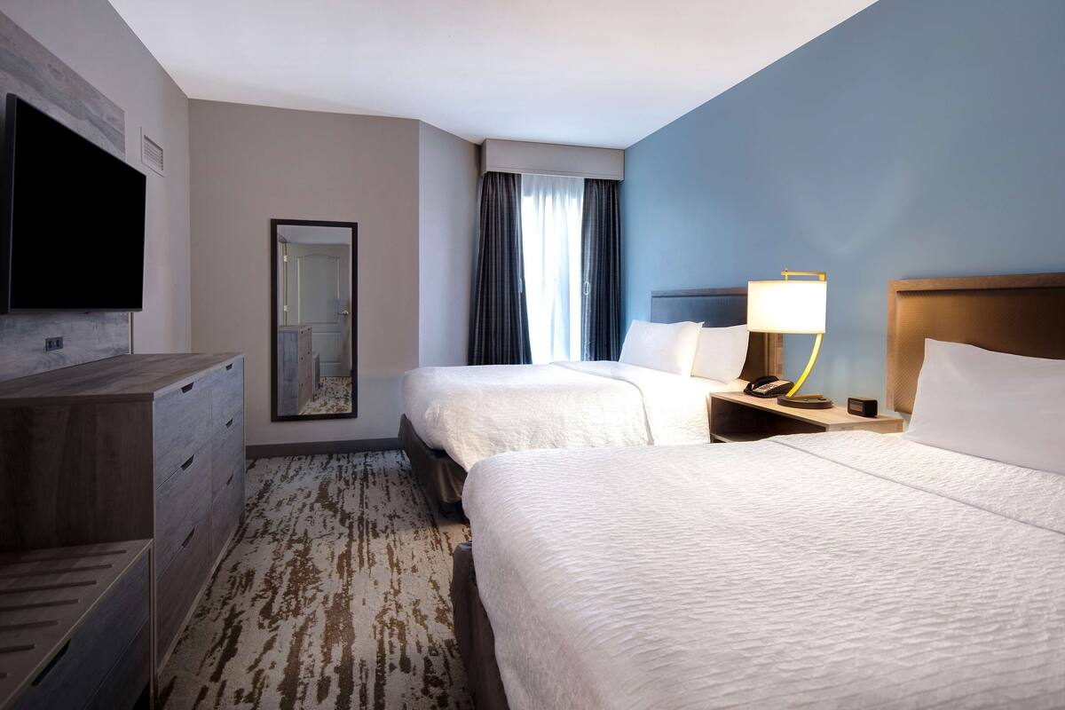 A hotel room with two beds, a TV, a desk, and a mirror.