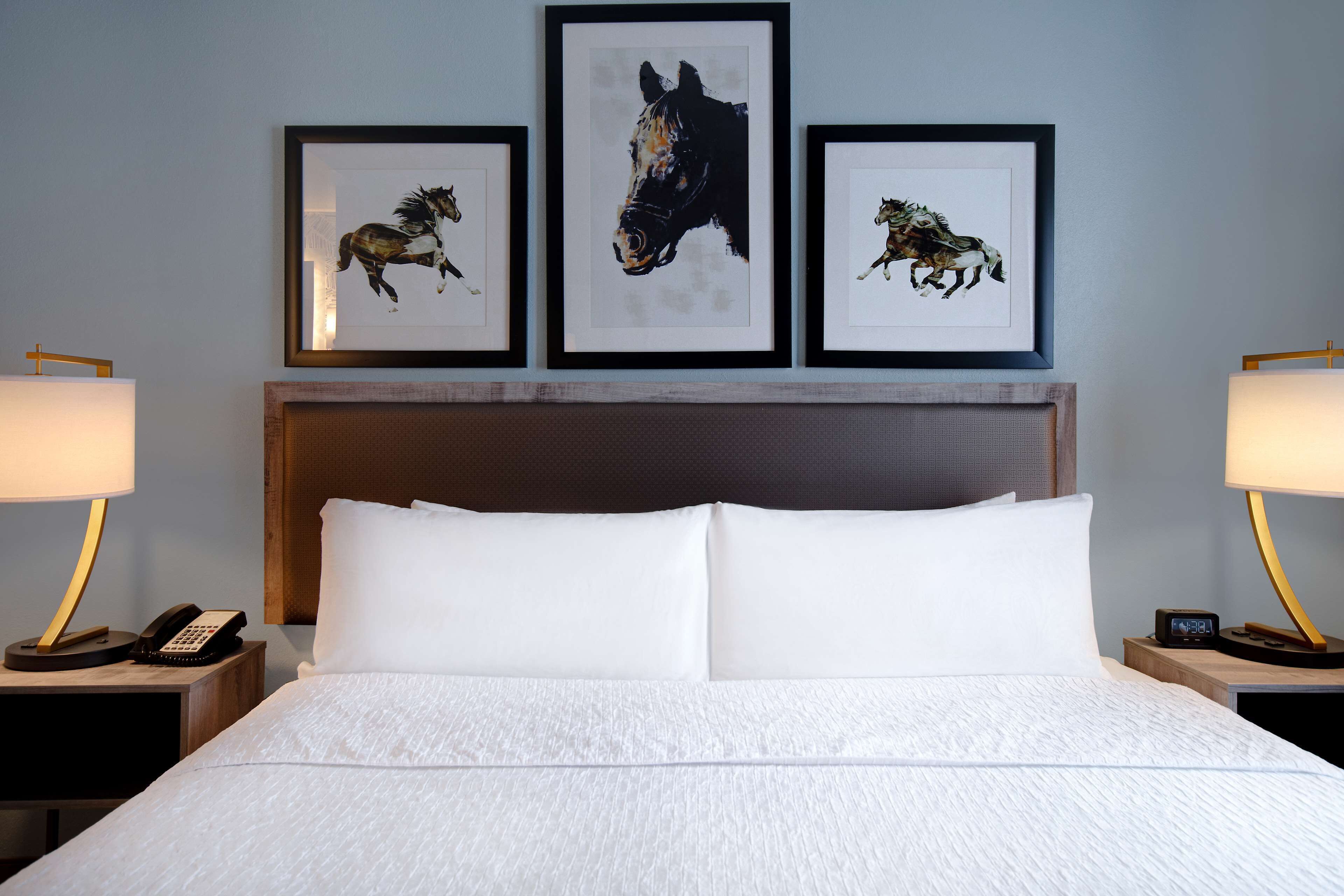 Ein Hotelzimmer mit einem großen Bett, weißer Bettwäsche, einem hölzernen Kopfteil und drei gerahmten Bildern von Pferden an der Wand.