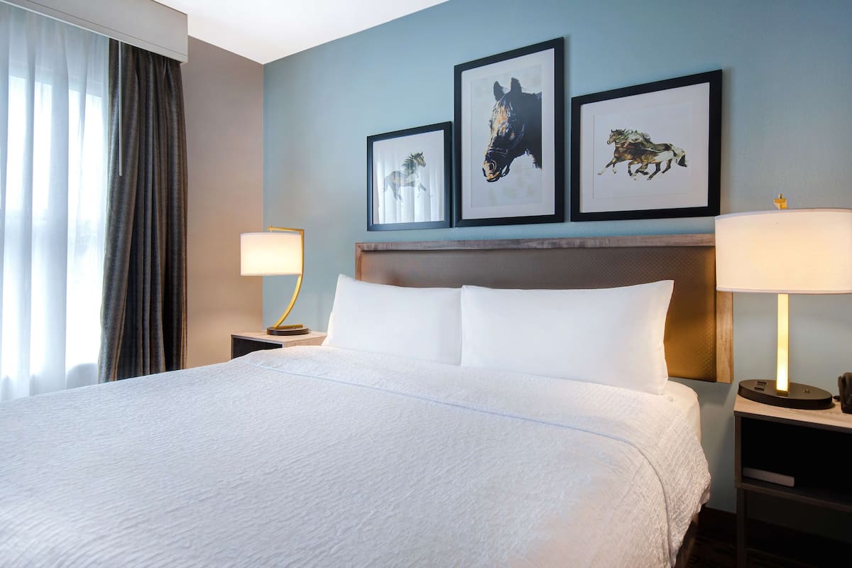 A hotel room with a large bed, two bedside tables with lamps, a headboard, and three framed pictures on the wall.
