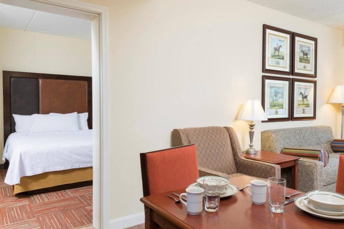 A hotel room with a bed, a dining table set with plates, glasses, and a teapot, a sofa, and a lamp.