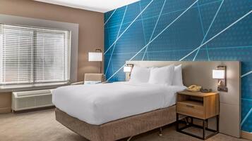 Une chambre d’hôtel avec un lit, des tables de chevet, un radiateur et une fenêtre avec des stores.