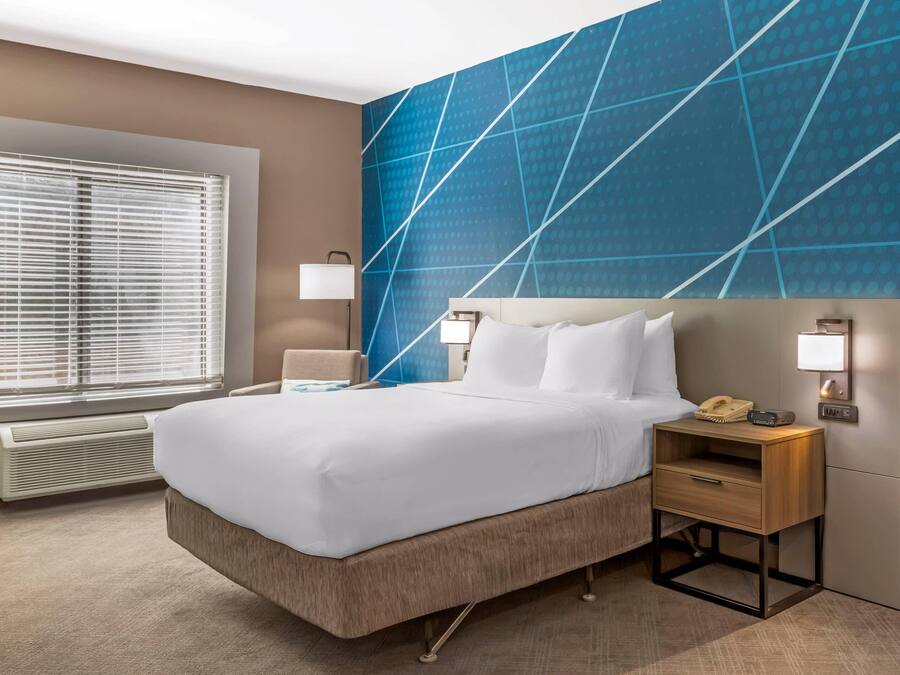 Une chambre d’hôtel avec un lit, des tables de chevet, un radiateur et une fenêtre avec des stores.