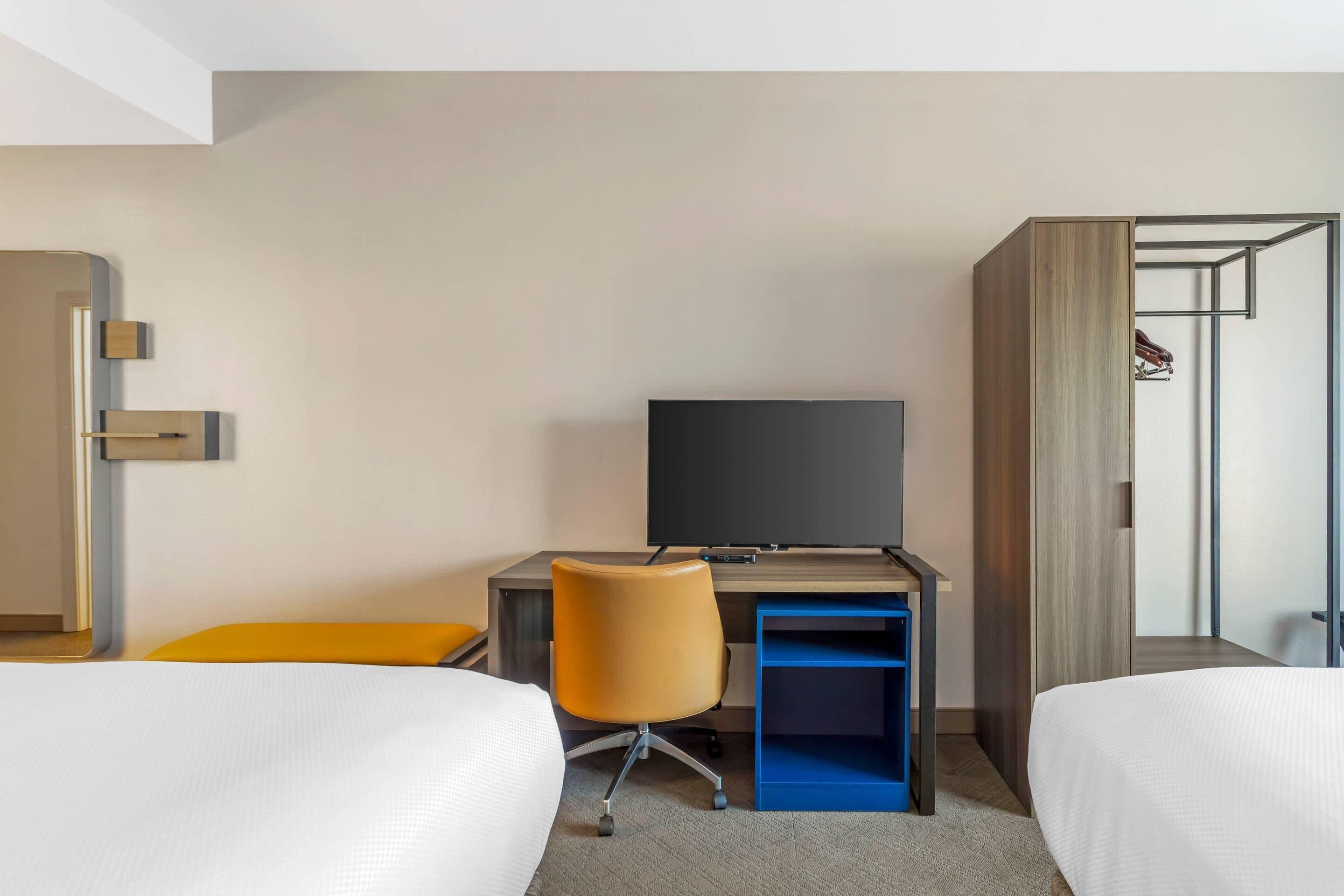 Une chambre d’hôtel avec deux lits, un bureau avec une télévision et une armoire.