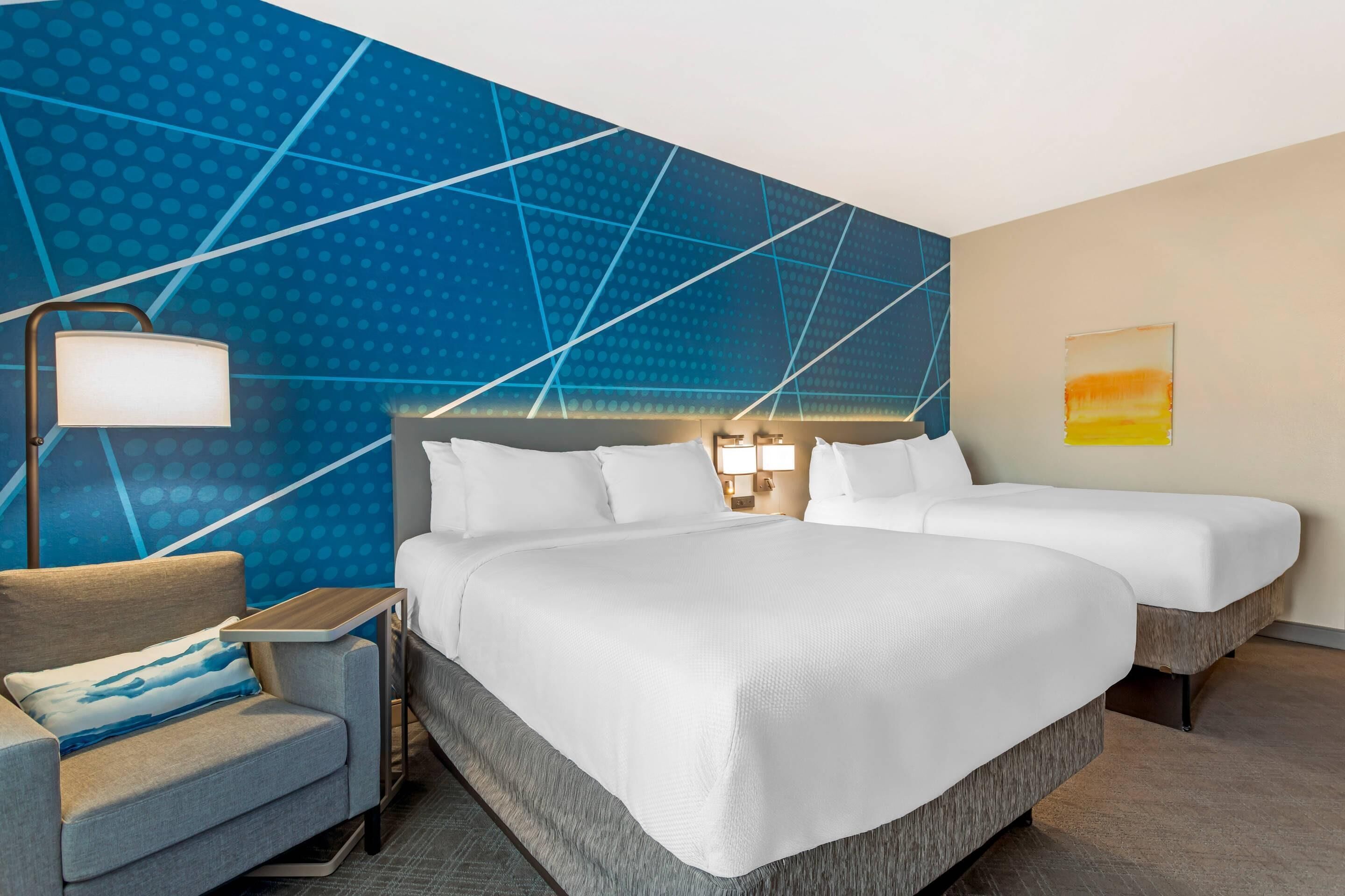 Ein Hotelzimmer mit einem großen Bett, zwei Nachttischen, einem Schreibtisch und einem Stuhl.