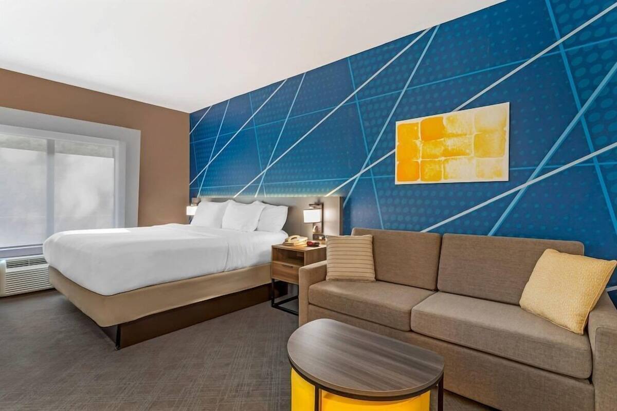 A hotel room with a bed, a sofa, a nightstand, a lamp, and a wall with geometric patterns.
