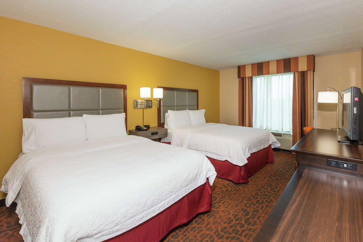 Une chambre d’hôtel avec deux lits, un bureau, une télévision et une fenêtre avec des rideaux.