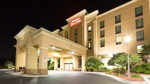 A Hampton Inn & Suites with a clear entrance, outdoor seating, and a well-lit facade.