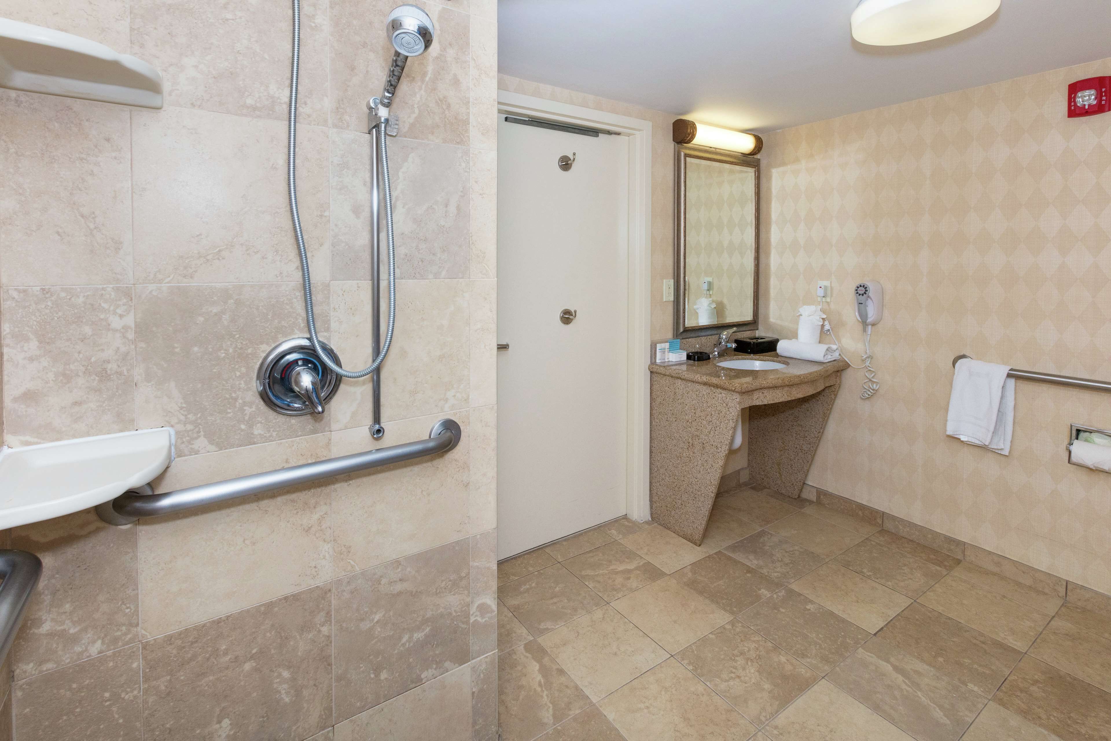 A bathroom with a shower, a sink, a mirror, and a hand dryer.