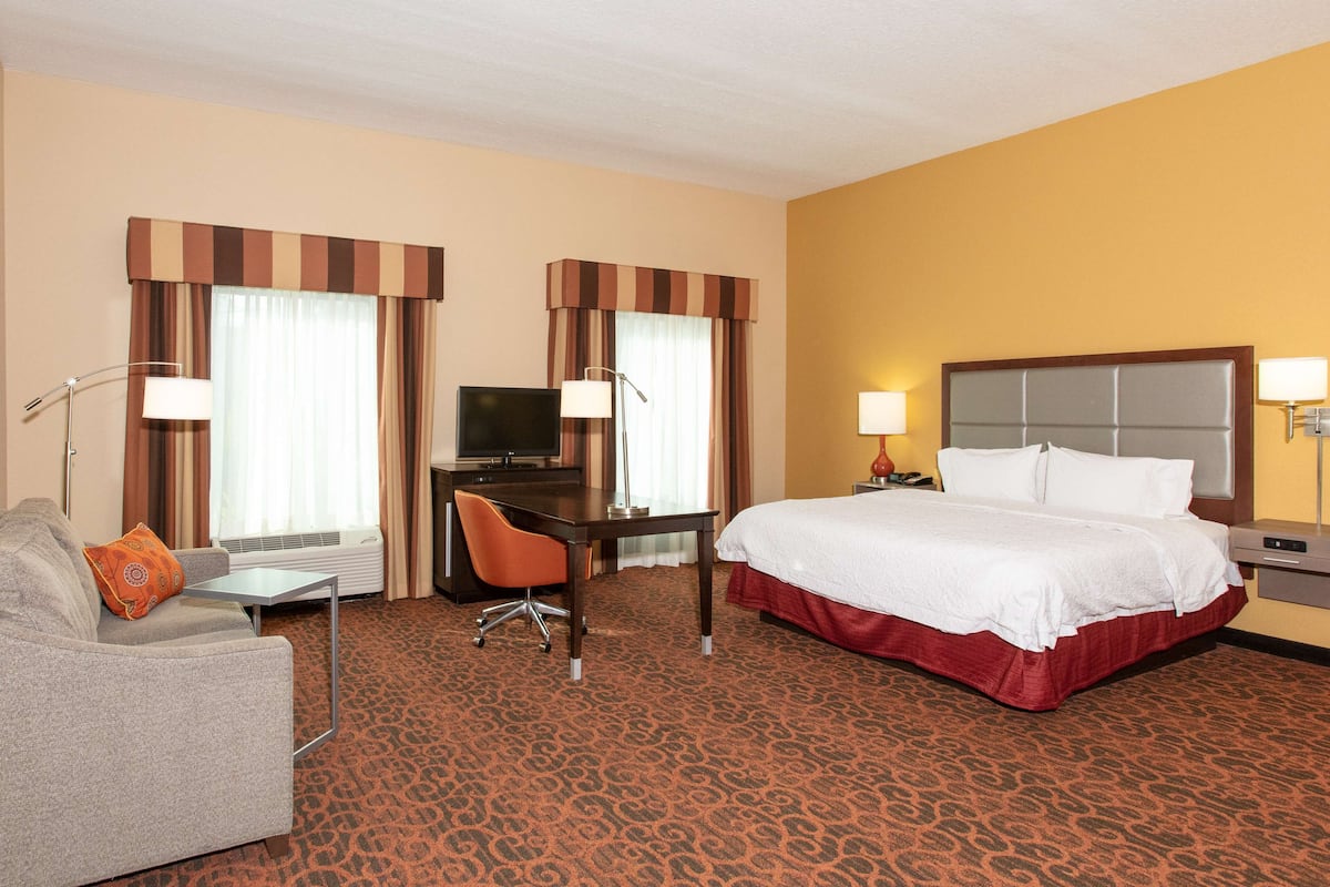 Une chambre d’hôtel avec un lit, un bureau, une chaise, un canapé et un téléviseur.