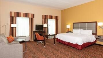Una habitación de hotel con cama, escritorio, sillón, sofá y televisor.