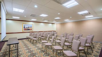 Un salón de conferencias con filas de sillas, una pantalla de proyector y suelo alfombrado.