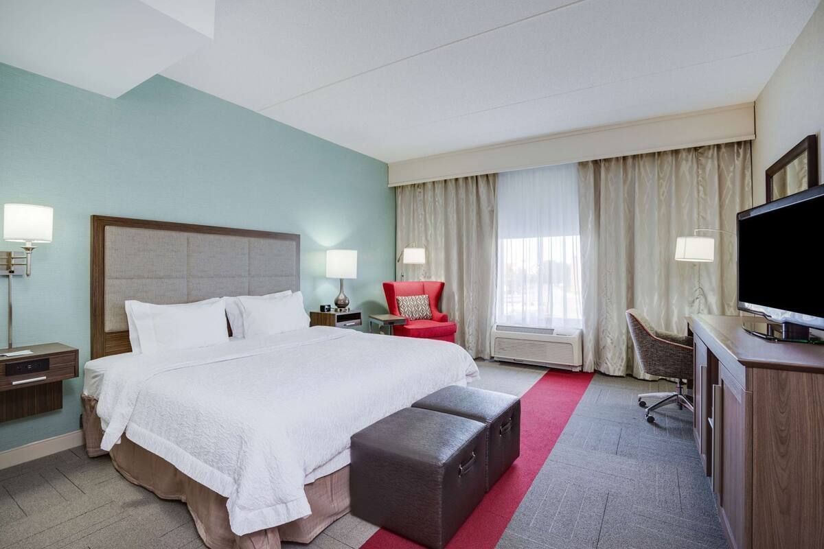 Habitación de hotel con una cama grande, un escritorio con televisor de pantalla plana, una silla roja y una ventana con cortinas.