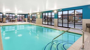 An indoor swimming pool with clear blue water, a tiled deck, and a view of the outside building.
