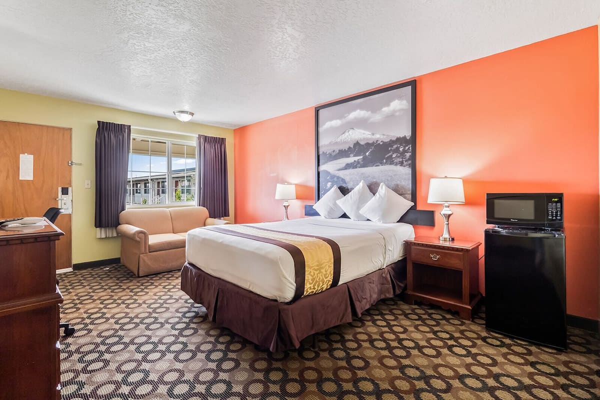 Een hotelkamer met een bed, een bureau, een stoel, een televisie en een raam met gordijnen.