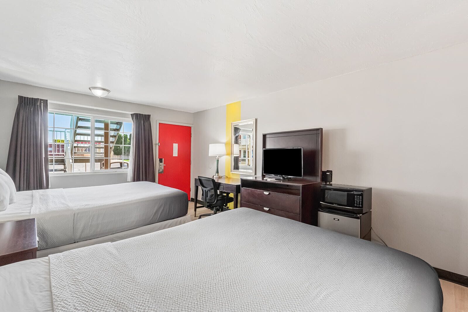 A hotel room with two beds, a desk with a chair, a TV, and a microwave.