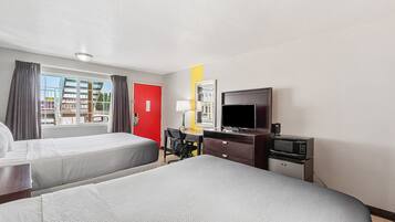 A hotel room with two beds, a desk with a chair, a TV, and a microwave.