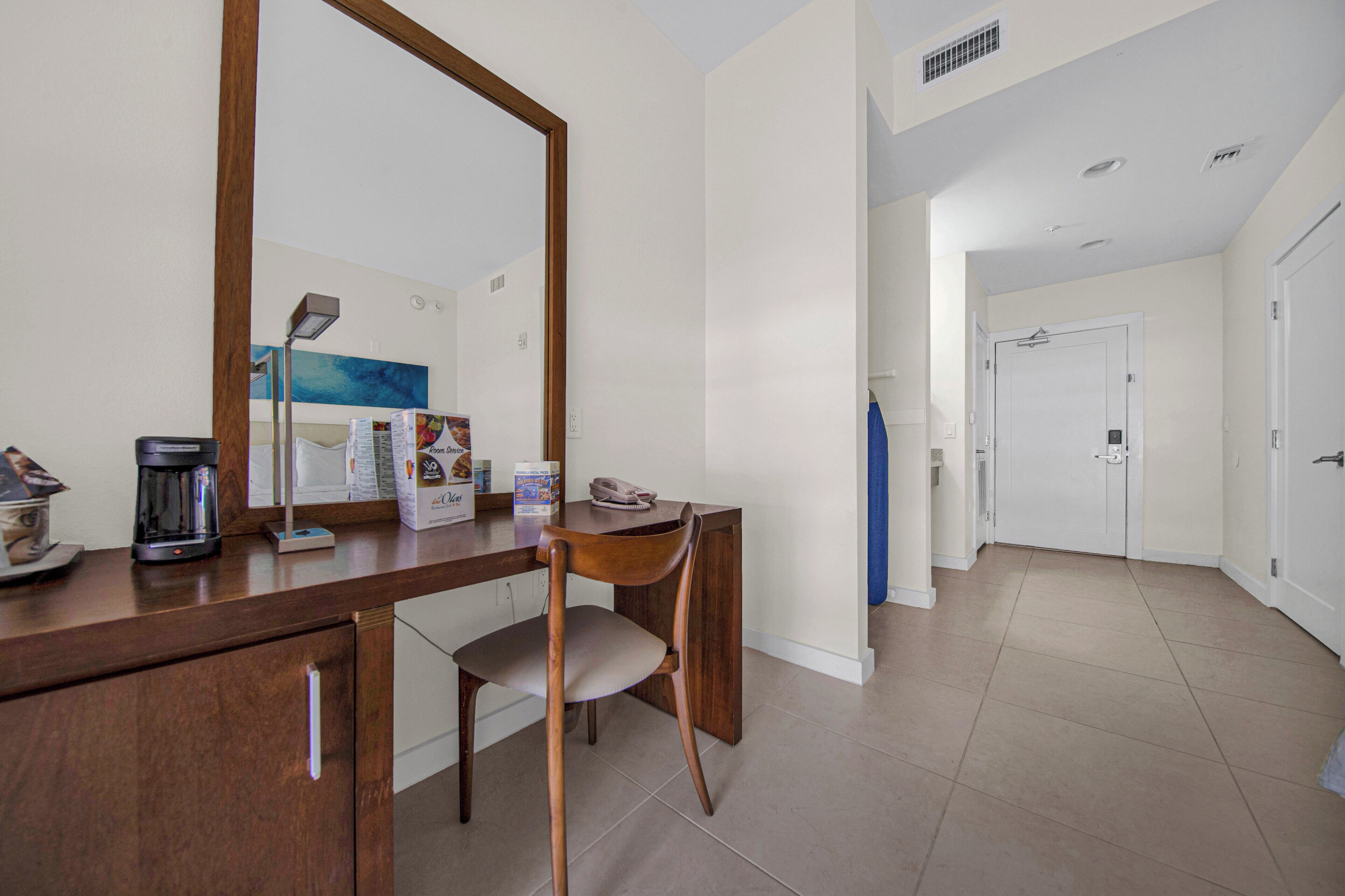 Una camera d'albergo con una scrivania in legno, una sedia, uno specchio grande e una porta che dà su un'altra stanza.