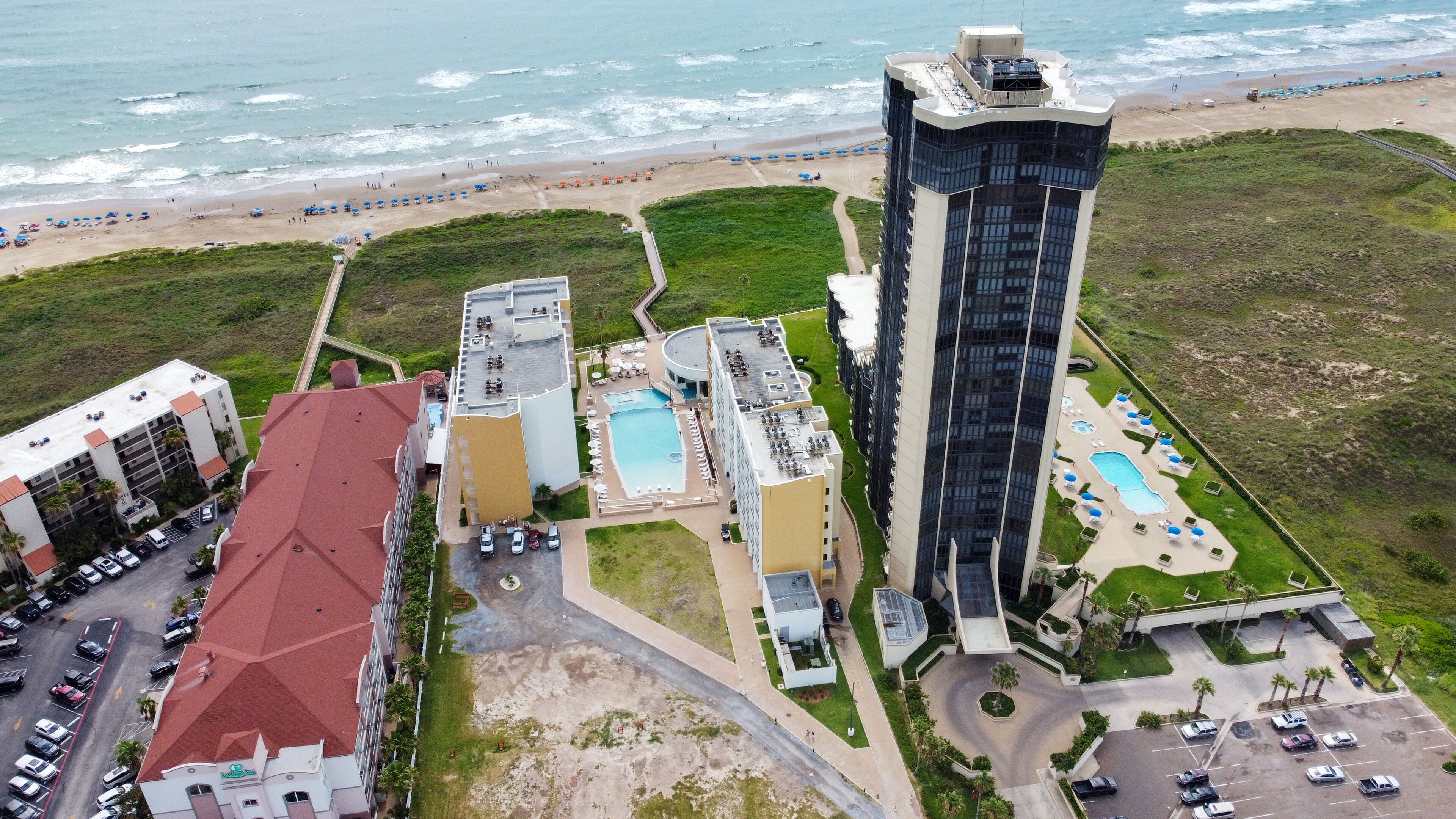Un hôtel de grande hauteur doté d’une piscine sur le toit, situé à côté d’une plage parsemée de parasols.
