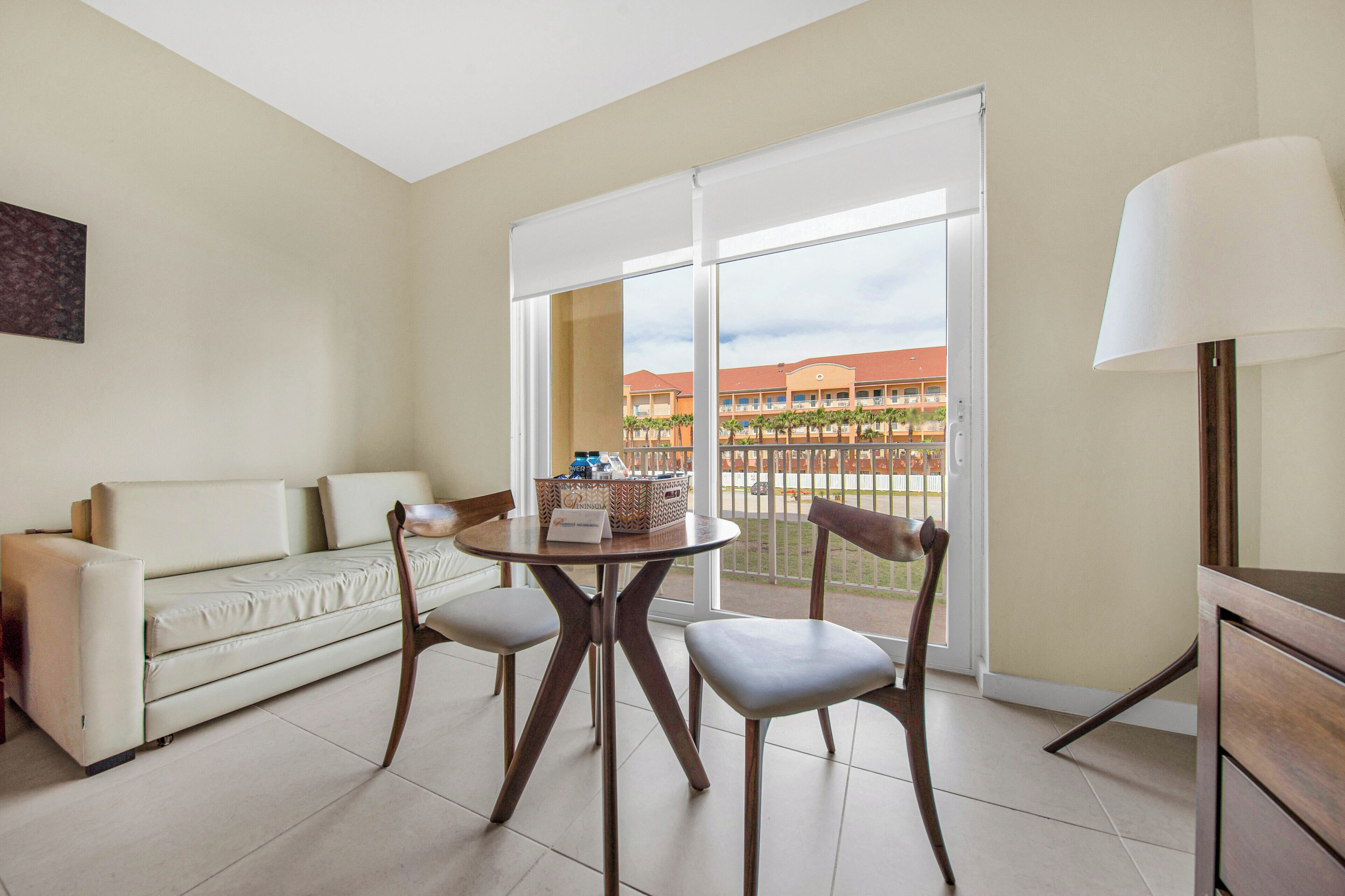 A room with a sofa, two chairs, a table with a basket, and a lamp.